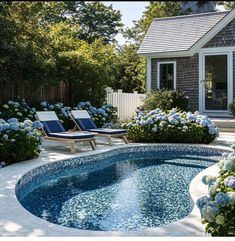 a small pool surrounded by blue hydrangeas and lawn chairs in front of a house