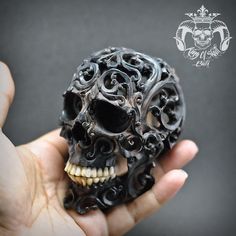 a hand holding a small black skull with intricate carvings on it's face and teeth
