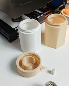 two cups sitting next to each other on top of a white table with an electronic device in the background