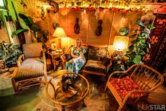 a woman sitting on a chair in a living room filled with lots of plants and furniture