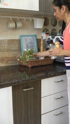 a woman standing in a kitchen preparing food on top of a wooden counter next to a potted plant