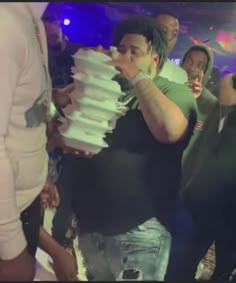 a man holding a stack of cake in front of his face while others look on
