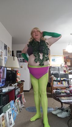 a woman dressed in green and purple is standing on the floor with her hands behind her head