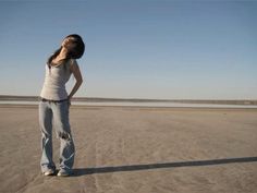 a woman is standing on the beach with her hands behind her head and eyes closed