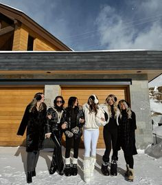 four women standing in front of a garage with snowboards and skis on their feet