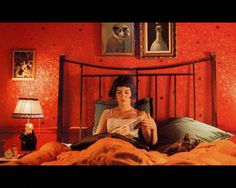 a woman sitting on top of a bed in a room with red walls and paintings