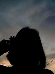 the silhouette of a person holding a cell phone up to their ear, against a cloudy sky