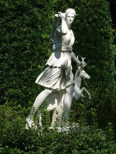 a statue of a woman holding a deer in front of some bushes and trees,