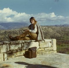 a woman sitting on top of a stone wall with her legs crossed and wearing boots