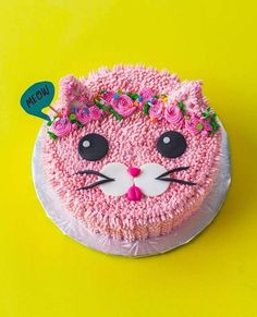 a cake decorated with pink frosting and flowers on top of a yellow tablecloth