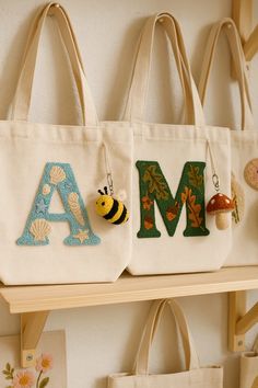 two tote bags are hanging on the wall with letters and a bee in it