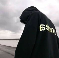 a person wearing a black hoodie with the word esnt printed on it, standing in front of a white wall