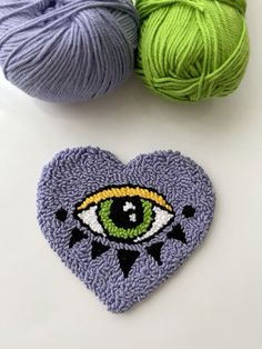 two balls of yarn next to a crocheted heart with an eye on it