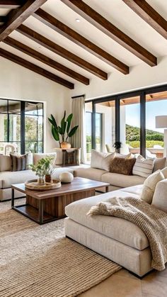 a living room filled with lots of furniture next to large windows and wooden beams