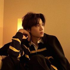 a young man sitting on top of a couch wearing a black and yellow striped sweater
