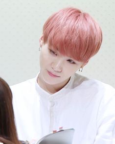 a young man with pink hair is looking at another person's reflection in the mirror