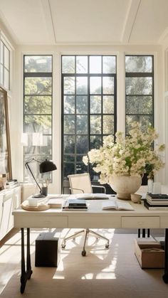 a white desk in front of two large windows and a vase with flowers on it