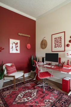 an office with red walls and rugs on the floor in front of a computer desk
