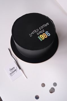 a black cake sitting on top of a white table next to a pen and paper
