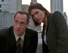 a man and woman in business attire posing for the camera with city buildings in the background
