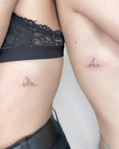 two women with small tattoos on their stomachs, one has a sailboat tattoo