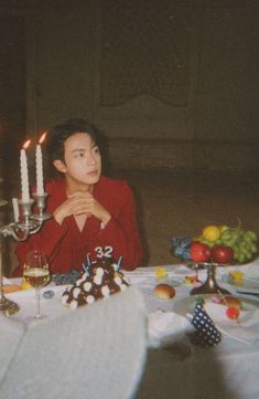 a woman sitting at a table with candles in front of her and fruit on the table
