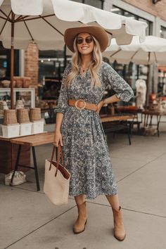 A summer western outfit with a floral midi dress, a leather belt, and tan ankle boots.