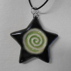 a green and black star shaped pendant with a spiral design on it's side