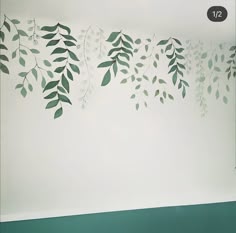 the wall is painted with green leaves and branches on it, along with white walls