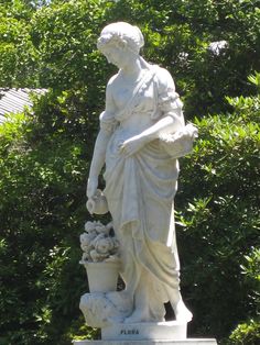 a statue holding a potted plant in front of some trees