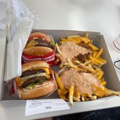 two hamburgers and french fries in a box with some ketchup on the side