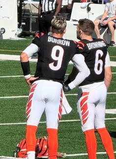 two football players standing next to each other on top of a field with people in the background
