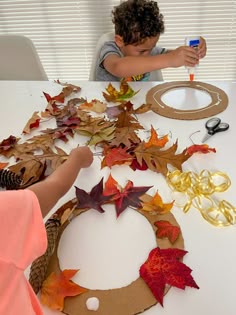 a young boy is making a wreath out of paper leaves and other autumn decorations on a table