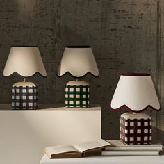 three lamps sitting on top of a table next to an open book and lamp shade