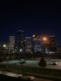 the city skyline is lit up at night with cars driving on the road in front of it