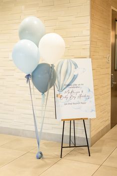 a sign with balloons attached to it in front of a brick wall and door way