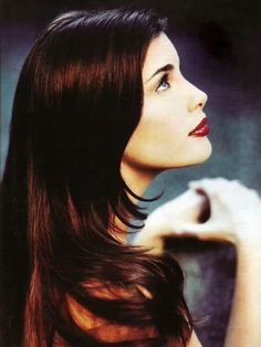 a woman with long brown hair and red lipstick is posing for the camera while holding her hand on her shoulder