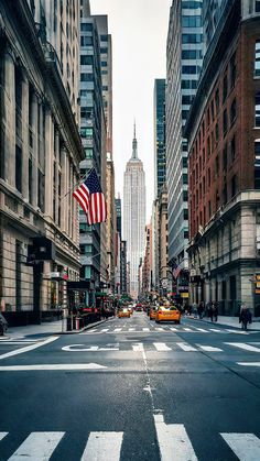 an american flag is flying in the middle of a busy city street with tall buildings