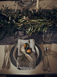 a place setting with silverware, napkins and greenery on the table top