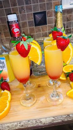 three glasses filled with orange juice and strawberries on top of a wooden cutting board