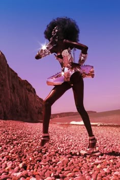 a woman standing on top of a rocky beach next to the ocean with an afro wig