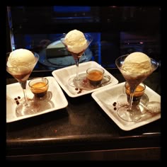 three dessert dishes with ice cream in them on a black countertop next to some drinks