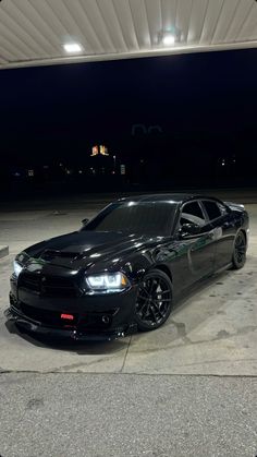 a black car is parked in the parking lot at night time with its lights on