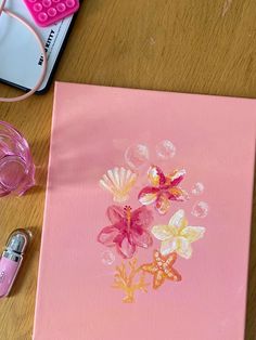 a pink canvas with flowers painted on it next to some glasses and a cell phone