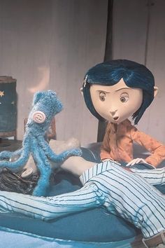 two dolls sitting on top of a bed next to an octopus and a stuffed animal
