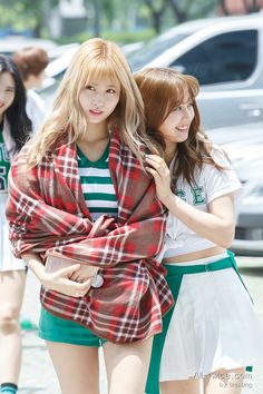 two young women are walking down the street with their arms around each other and one is wrapped in a plaid blanket