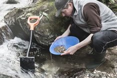 a man kneeling down next to a river holding a blue bowl with food in it