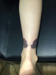 a woman's foot with an angel wing tattoo on her left leg and black leather chair in the background