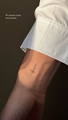 a person's arm with a small cross tattoo on the left side of their arm
