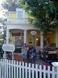 a yellow house with antiques on the front porch and in the back yard is a white picket fence